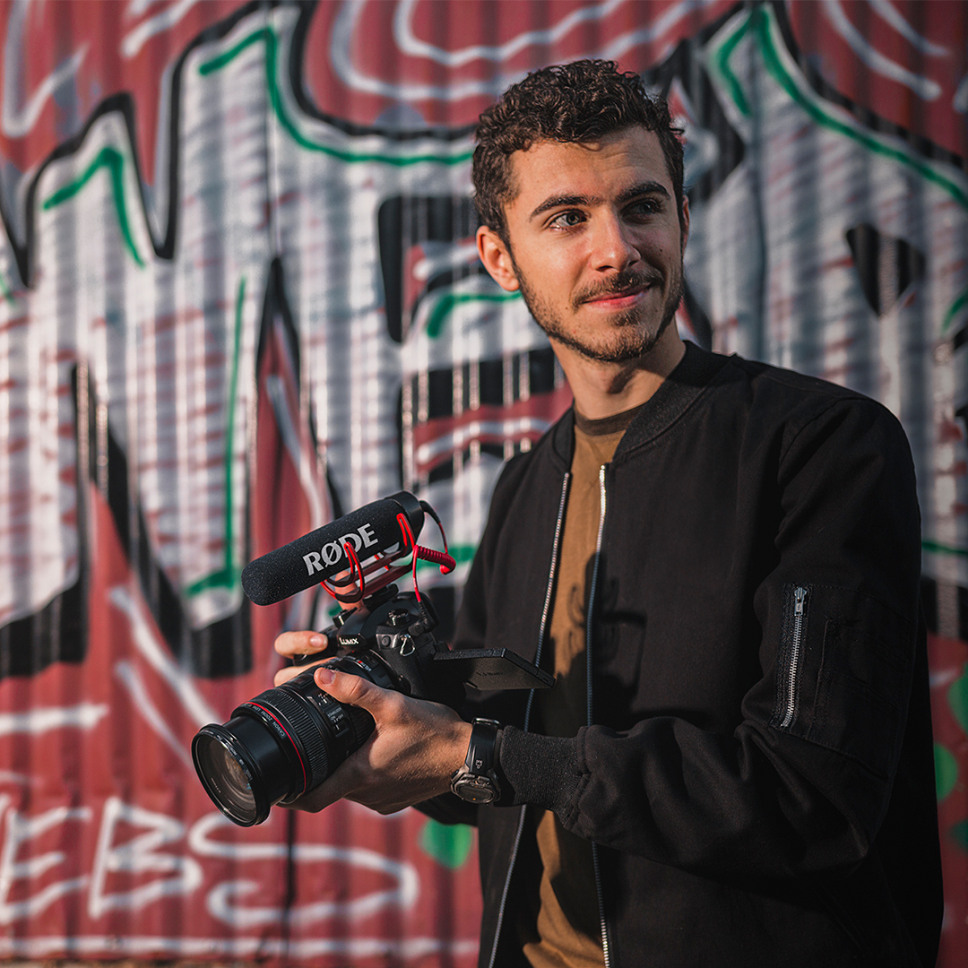 man standing in front of graffiti wall with camera and videomic go mounted on top.