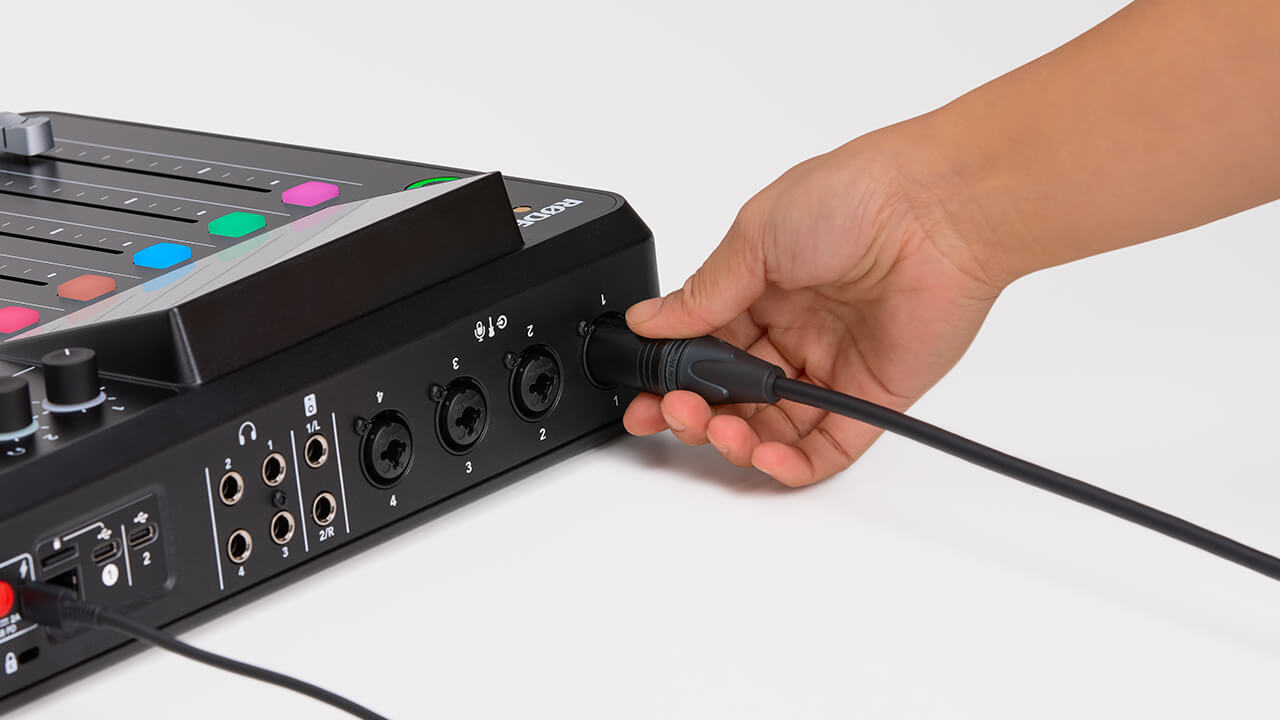 Hand connecting XLR cable to back of RØDECaster Pro II